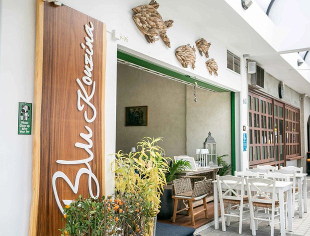 Breezy Greek-themed restaurant with sustainable wood furniture, light blue tones, and rattan ceiling lights by Theodora Martinou from Irregular Lines.