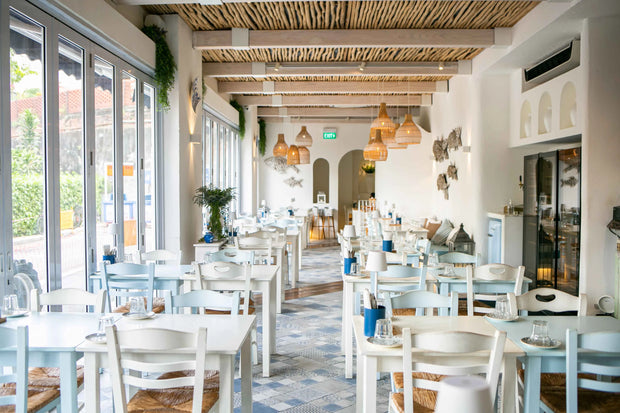 Authentic Mediterranean dining space with all-natural materials, light blue accents, and rattan lighting designed by Theodora Martinou of Irregular Lines.